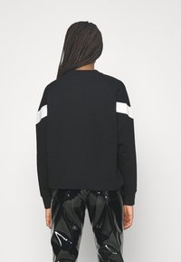 Zwarte sweatshirt met witte diagonale strepen op de mouwen, gemaakt van een zachte stof, gecombineerd met glanzende zwarte broeken.