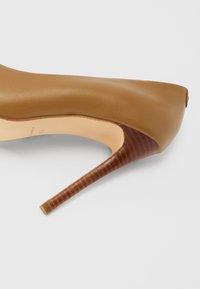 Brun læderhøjhælet sko med spids tå, med en struktureret mørkebrun hæl og en glat, mat finish på overdelen.