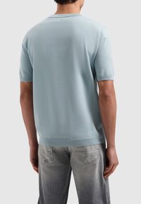 Lichtblauwe trui met korte mouwen en een ribbelhalslijn en -zoom. Gladde textuur en relaxte pasvorm, weergegeven van achteren.