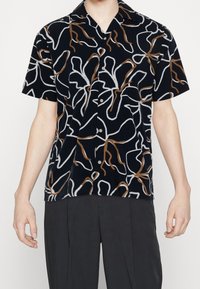 Košile s krátkým rukávem z tmavě modré látky s bílým a hnědým abstraktním vzorem čar, s zapínáním na knoflíky a klopovým límečkem.