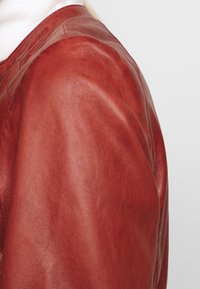 Röd läderjacka med en slät yta och en något figursydd design, med rundad nacke och sömnadsdetaljer längs sömmarna.