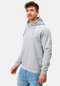 Sudadera gris con bolsillo tipo canguro y capucha con cordón. Presenta puños y bajo de canalé, con acentos naranjas y logo en la parte frontal.
