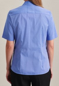 Kortärmad blå skjorta med en strukturerad krage, en mjuk textur och paneldetaljer på baksidan, kombinerad med svarta byxor.
