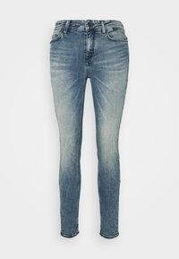 Jeans skinny azules desvanecidos exhibidos sobre un fondo blanco liso, con un diseño clásico de cinco bolsillos y cierre de cremallera.