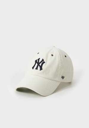 Witte corduroy honkbalpet met een marineblauw NY-logo op de voorkant, metalen oogjes en een klein marineblauw '47' op de zijkant.
