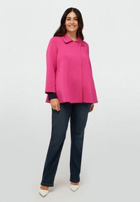 Fuchsia oversized jacka med krage, sidofickor och trekvartslånga ärmar, i kombination med mörkblå jeans och vita klackar.