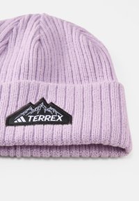 Purple ribbed knit beanie featuring a black patch with a mountain graphic and "TERREX" text. Soft texture, fold-over cuff design.