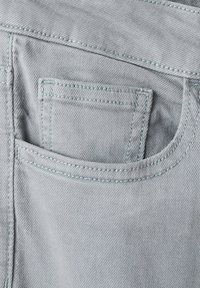 Jasnoszary materiał dżinsowy pokazujący górną część tylnej kieszeni z widocznym przeszyciem oraz mniejszą kieszonką w środku.