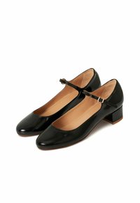 Zapatos de charol negros con punta redonda, tira en el tobillo y tacón bajo en bloque. El interior cuenta con un suave forro beige.