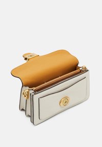 Petit sac en cuir beige avec fermeture à loquet doré, rabat ouvert révélant un intérieur beige et un compartiment zippé à l'intérieur.