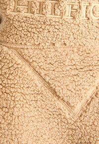 Beige fleece fabric with textured, curly wool-like surface and visible seam lines forming geometric patterns.