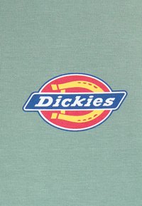 Green fabric t-shirt featuring a circular logo with "Dickies" in white, blue background, and red accents, highlighted by yellow design elements.