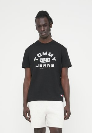 Čierne bavlnené tričko s okrúhlym výstrihom a krátkymi rukávmi. Obsahuje biely nápis "TOMMY JEANS" a logo na leme.