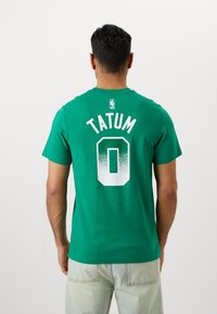 Green cotton T-shirt featuring "TATUM" and the number "0" on the back in white gradient text. Short sleeves, crew neckline, relaxed fit.