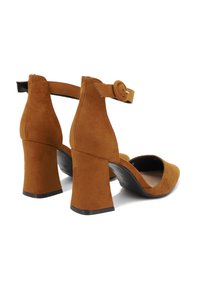 Elevati in suede marrone con tacco a blocco spesso e cinturino alla caviglia. Presentano un design a punta e una fodera interna liscia.