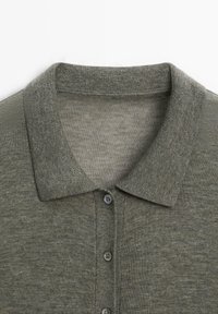 Polo-Shirt in gedämpftem Olivgrün, aus Strickstoff mit einem Kragenhals, einer Drei-Knopf-Verschlussleiste und gerippten Manschetten. Glatte Textur.