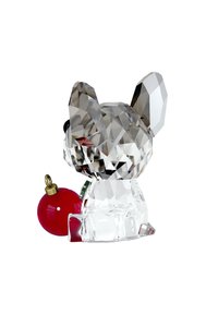 Przezroczysta figurka psa z kryształu o geometrycznych fasetach, zdobiona czerwoną ozdobą z złotym akcentem, prezentująca skomplikowane refleksy światła.