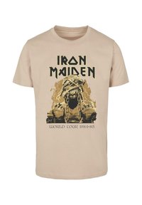 Beige bomulds t-shirt med et grafik af et skelet i kæder, med "Iron Maiden" ovenfor og "World Tour 1984-85" nedenfor i sort.