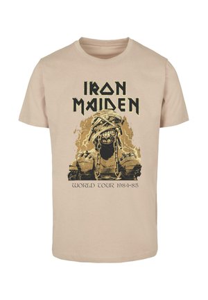 Béžové bavlnené tričko s grafikou kostry v reťaziach, s nápisom "Iron Maiden" nad a "World Tour 1984-85" pod ním v čiernej farbe.