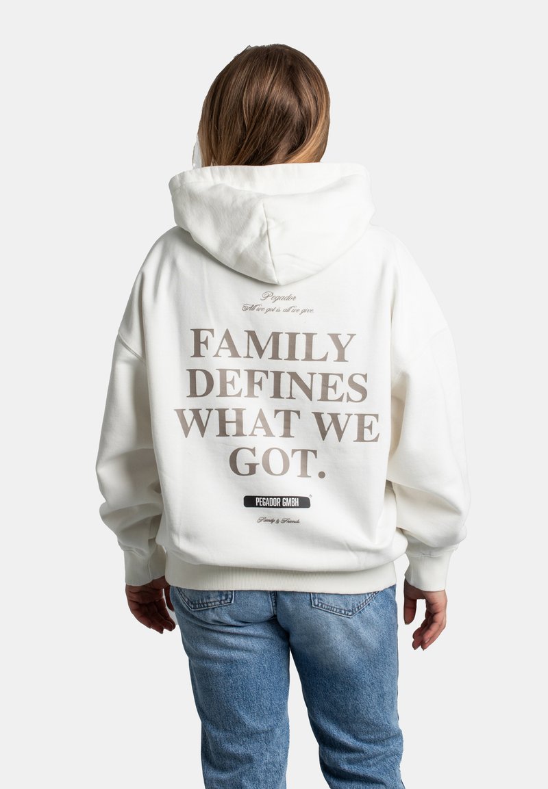 Bílá mikina s kapucí a oversized střihem. Na zádech je velký nápis: "FAMILY DEFINES WHAT WE GOT." a značková etiketa na lemu.