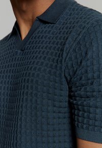 Navy getextureerde polo shirt met een V-hals, korte mouwen en een kenmerkend geweven patroon, gemaakt van een zachte breisel stof.