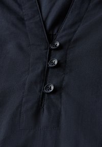 Camisa azul marino con escote en V, que presenta una tapeta y cuatro botones negros. Tejido suave con un brillo sutil y detalles de costura limpios.