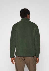 Dark green fleece jacket with a high collar, textured surface, and zippered front. Features elastic cuffs and a straight hem.
