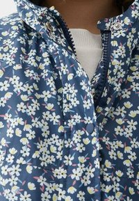 Floral jacket with a navy blue background, featuring small white and yellow flowers with pink accents. Front zip closure and snap buttons.