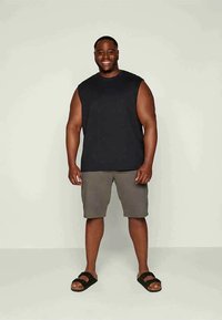 Camiseta preta sem mangas combinada com calções cinzentos. Os calhões são até aos joelhos e o conjunto é complementado por sandálias pretas.