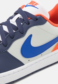 Nike sneakers featuring a navy and light gray leather upper, blue swoosh, orange accents, and textured laces on a white rubber sole.
