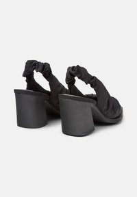 Scarpe nere con tacco alto e fasce di tessuto arricciato sul retro, che mostrano un tacco spesso e una suola liscia, presentate da un'angolazione leggermente inclinata.