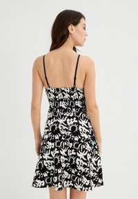 Vestido de verano con estampado en blanco y negro, con un corpiño fruncido y tirantes delgados ajustables, que se abre en una falda de largo hasta la rodilla. Vista desde atrás.
