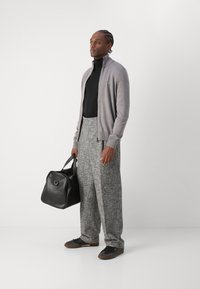 Grå zip-up kofta över en svart tunntröja, tillsammans med löst texturerade gråbyxor. En svart läderhandväska och mörka sneakers fulländar looken.