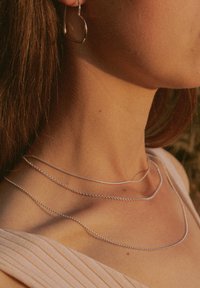Silberne geschichtete Halsketten mit einer glatten Kette, perlenförmigem Design und zarter Verarbeitung, getragen mit einem hellen Oberteil.