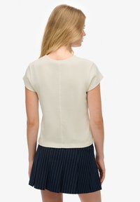 Top corto beige de manga corta con escote redondo, textura suave y una costura trasera recta, combinado con una falda plisada a rayas marino.