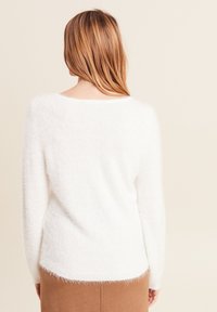 Maglione bianco morbido con scollo a barca e maniche lunghe. L'orlo è leggermente più lungo sul retro. Tessuto morbido e vestibilità ampia.