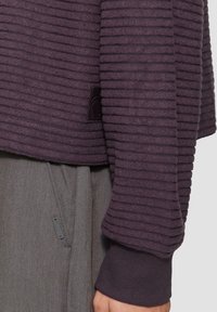 Paarse ribgebreide trui met textuurstrepen en een manchet mouw, gecombineerd met grijze stoffen broek met een ritszakdetail.