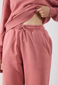 Pantaloni din bumbac roz, cu talie cu șnur, buzunare laterale și textură moale. Asortați cu un hanorac cu guler rotund.