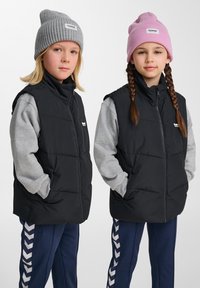 Zwei Kinder tragen ärmellose schwarze Steppwesten über grauen Langarmshirts, eines mit einer pinken Mütze und das andere mit einer grauen Mütze.