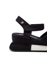 Sandalias de plataforma negras con un upper liso, correas ajustables y un acento blanco en una suela de cuña con una base texturizada para agarre.