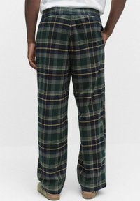 Gröna rutiga byxor med avslappnad passform, med blå och gula accenter, synliga sömmar och en mjuk textur, sedd från baksidan.