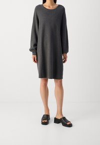 Abito grigio in maglia a maniche lunghe con scollatura rotonda, vestibilità rilassata e polsini a costine, abbinato a sandali neri con tacco a blocco.