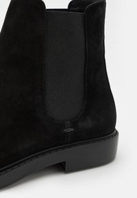 Bottine Chelsea en daim noir avec panneaux élastiques sur les côtés, semelle en caoutchouc lisse et détails de couture subtils.
