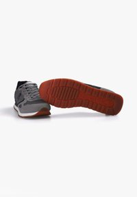 Zapatos deportivos para hombre con parte superior de malla gris y negra, acentos de ante gris texturizado y suela de goma con superficie naranja.