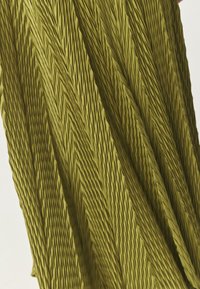 Grüner, strukturierter Stoff mit einem gefältelten Design, das eine Reihe von diagonalen Rillen und glatten Abschnitten aufweist, die visuelle Tiefe erzeugen.
