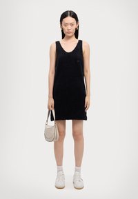 Black sleeveless dress with a fuzzy texture, featuring a deep V-neck and a straight cut. Paired with a light-colored handbag and white sneakers.