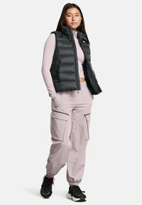 Gilet imbottito nero, maglietta a maniche lunghe rosa chiaro, pantaloni cargo rosa pallido con polsini elasticizzati e scarpe da ginnastica nere. Motivi e dettagli minimi.