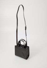 Sac à main en cuir noir avec une forme rectangulaire structurée, deux poignées supérieures et une bandoulière longue et réglable. Texture lisse et design minimaliste.