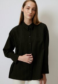 Dark green button-up shirt with white vertical stripes, featuring a pointed collar and long sleeves with cuff detail. Soft, textured fabric.