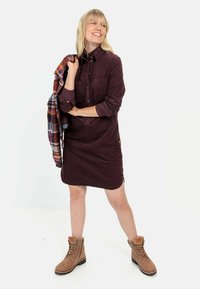 Brun corduroy skjorte kjole med knapper og krave, med en brystlomme. Parret med beige snørebånd støvler og en flerfarvet plaid jakke.
